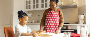 Black mom and daughter in a kitchen making cookies this holiday season.