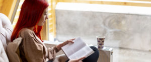 Teenager sitting by a window on a cold winter day reading a book with the headline "Prioritizing Your Mental Health: Indoor Self-Care".