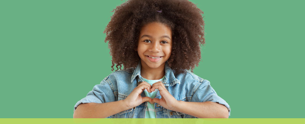 Black teen girl making a heart with her hands for World Kindness Day.