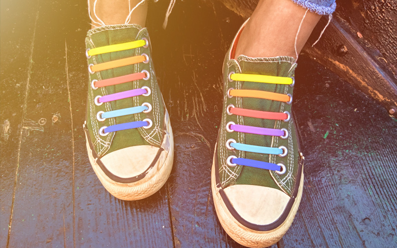 Teen feet and shoes with rainbow laces outside in summer.