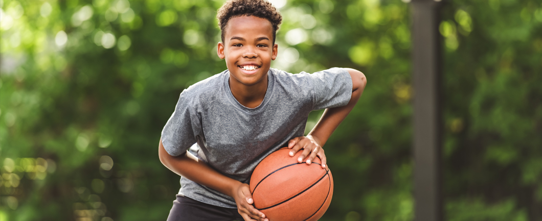 Young boy outside in summer having fun playing basketball.