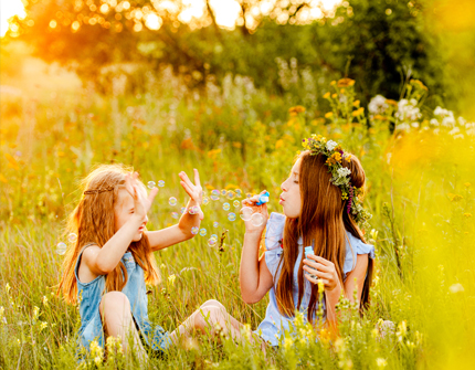 Girls sitting in a field in summer blowing bubbles and having fun.