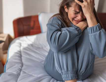 Teen girl sitting on her bed crying and appearing overwhelmed by emotional distress.