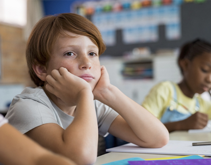 School-age boy sitting at his desk looking withdrawn and disengaged during class.